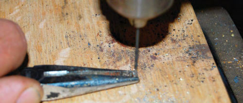 While holding the brass button with its neck up in needle nose pliers, the old wire and solder were carefully drilled out of the neck using a small bit in a drill press.