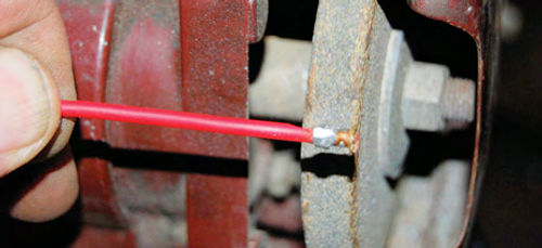 A glob of solder was dribbled on the gap between the red plastic wire insulation and the bottom of the brass button’s “neck” and a small grinder was used to shape the solder.
