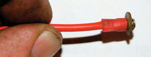 The plastic collar from a standard electrical connector was removed and used to better insulate the soldered connection and hold the fiber washer against the brass button.