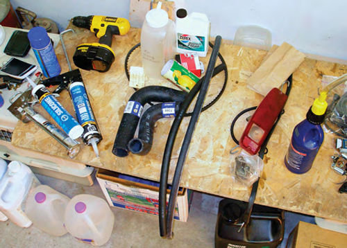 Photo 3. A fan belt, thermostat, hoses and radiator-flushing solution on the table—and antifreeze and distilled water stored on the floor—comprised my “cooling” inventory.