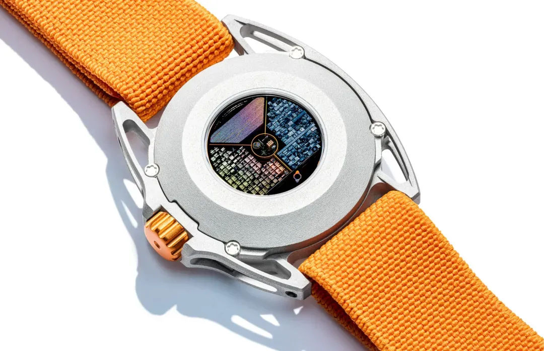 Barrelhand Monolith seen from the caseback on a white background: brushed aluminium back with an iridescent micro-etched Memory Disc at its centre, an orange fluted crown at nine o'clock, skeletonised lugs and an orange woven strap