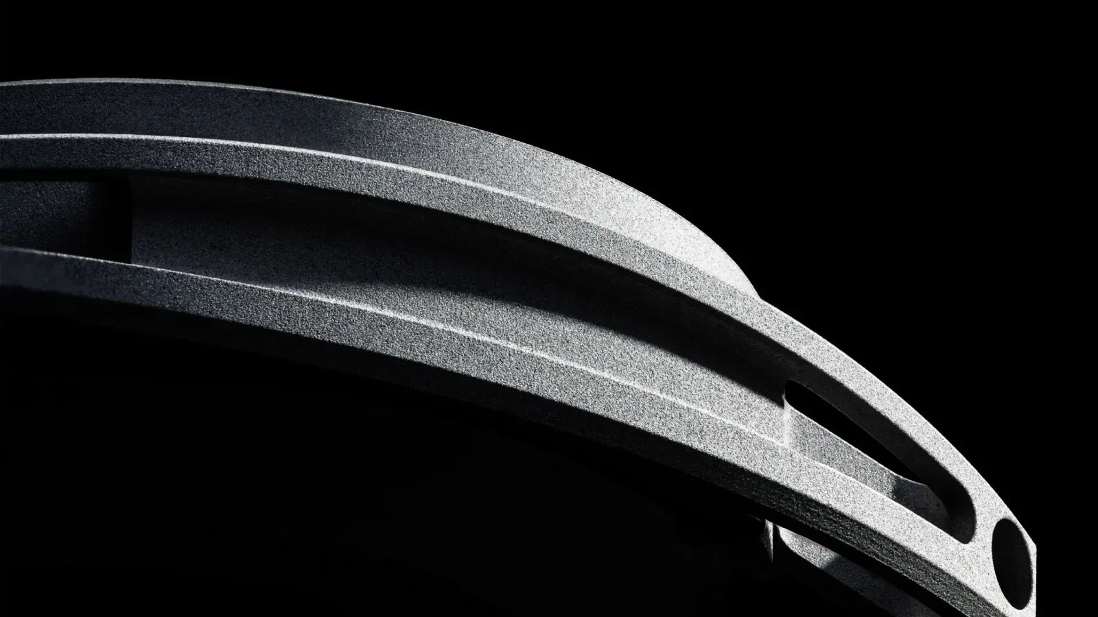 Macro shot of the printed Scalmalloy case wall against black, showing the grainy sintered surface and the hollow Aircore insulation channels running between the outer and inner walls