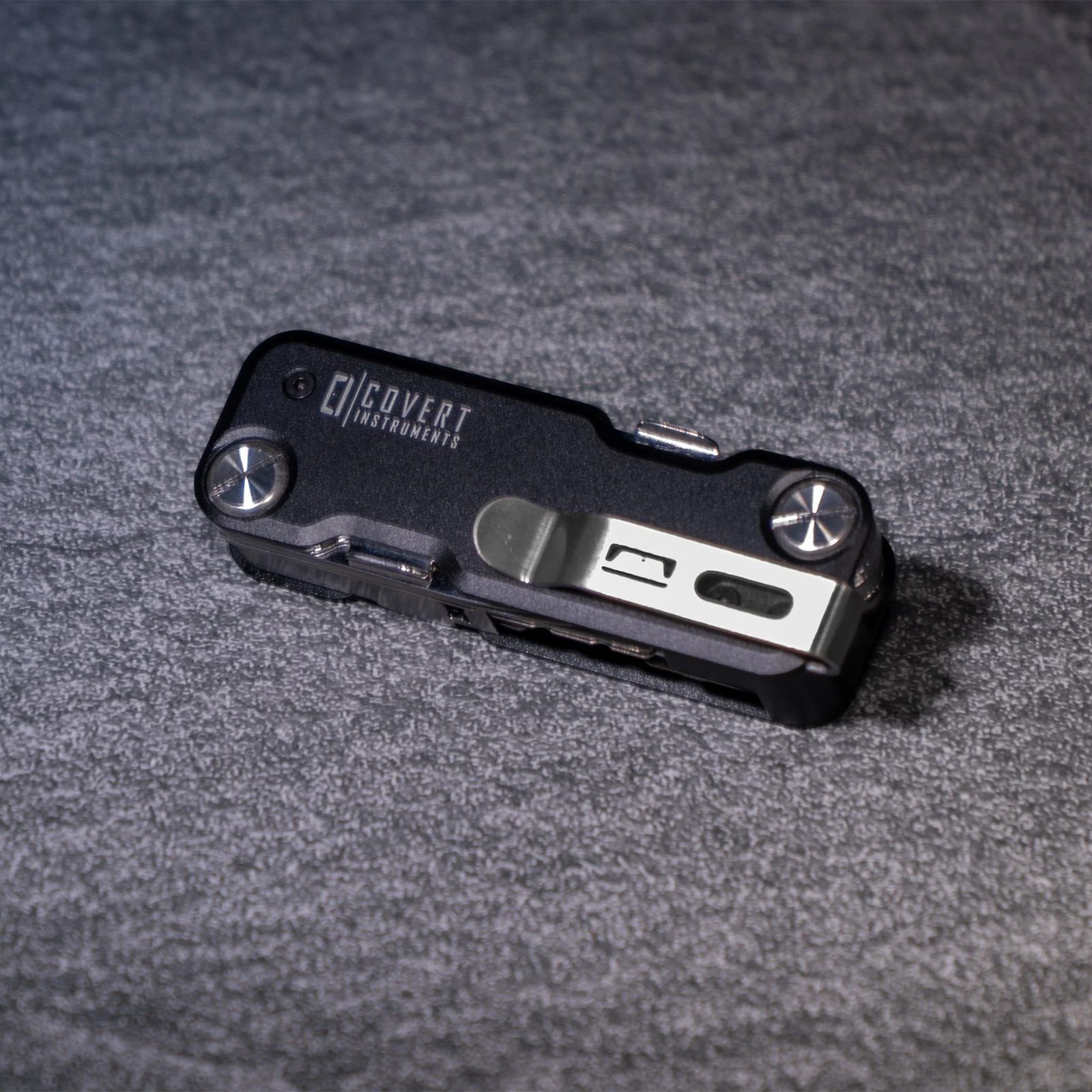 The Covert Companion Pro closed on a grey fabric surface, showing the black scales, the CI logo and the polished deep-carry clip