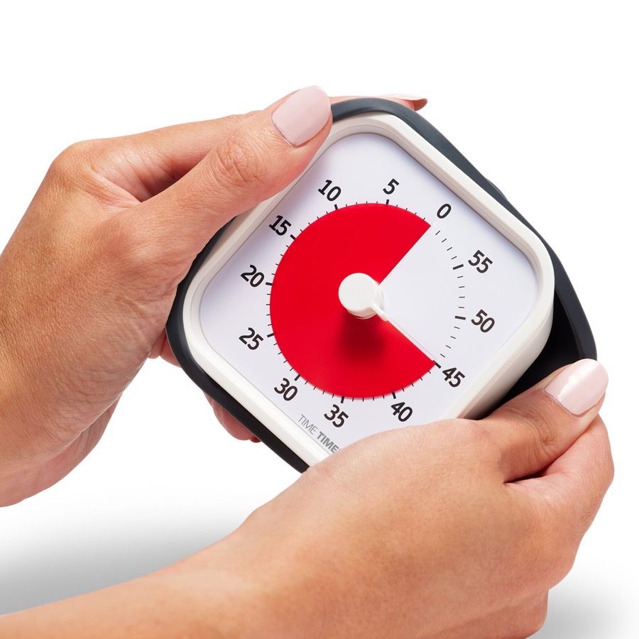 Two hands holding a Time Timer MOD, a rounded square timer with a white face and a red disk covering about half the dial, numbered 0 to 55