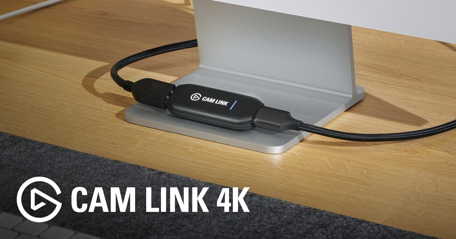 Elgato Cam Link 4K capture stick on a desk, connected between an HDMI cable and a monitor stand