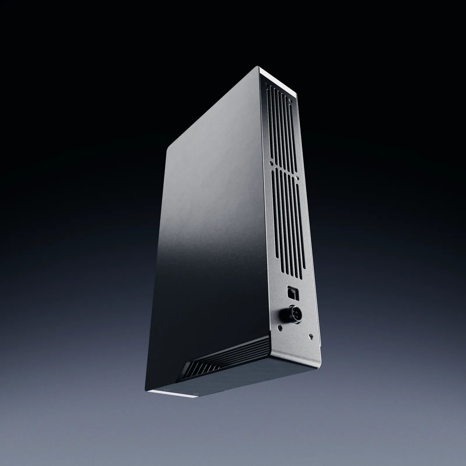 Ghost Core seen from the back three-quarter on a dark blue background: a tall black slab with a vertical vent grille and a round power socket on its rear panel