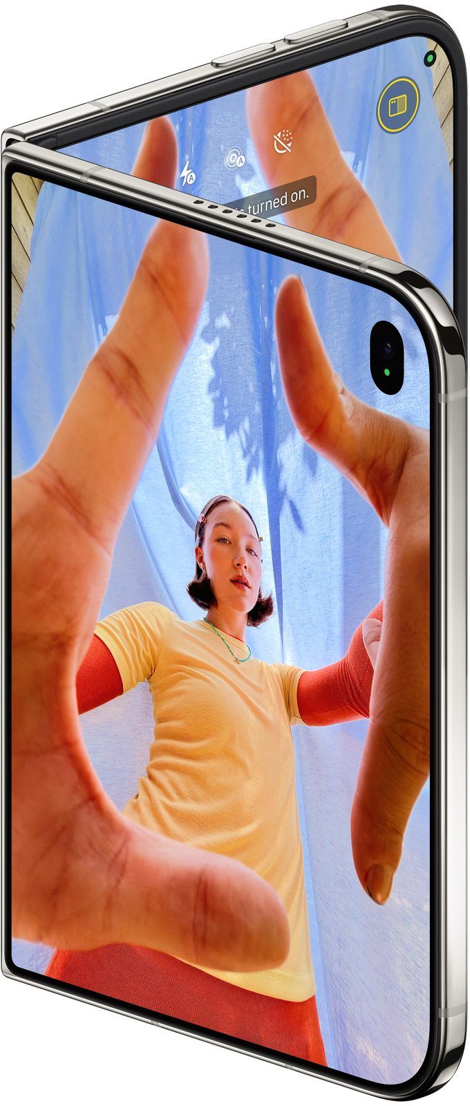 iPhone Duo closed, the outer display running the Camera app in selfie mode with a person framing a shot with their hands