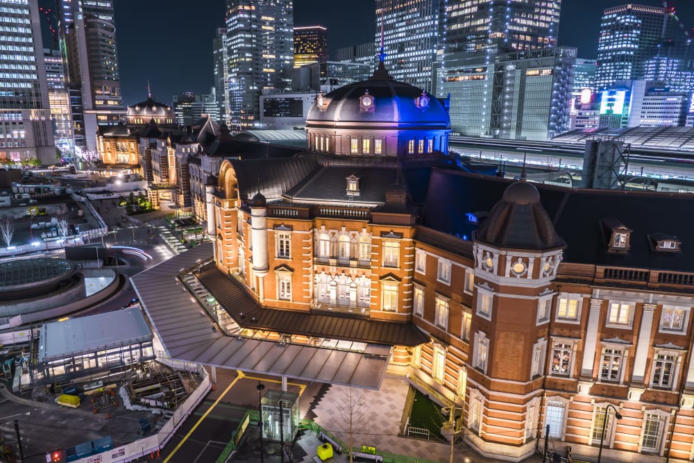 Tokyo Station's red-brick Marunouchi building lit up at night, its domes glowing blue, with office towers behind