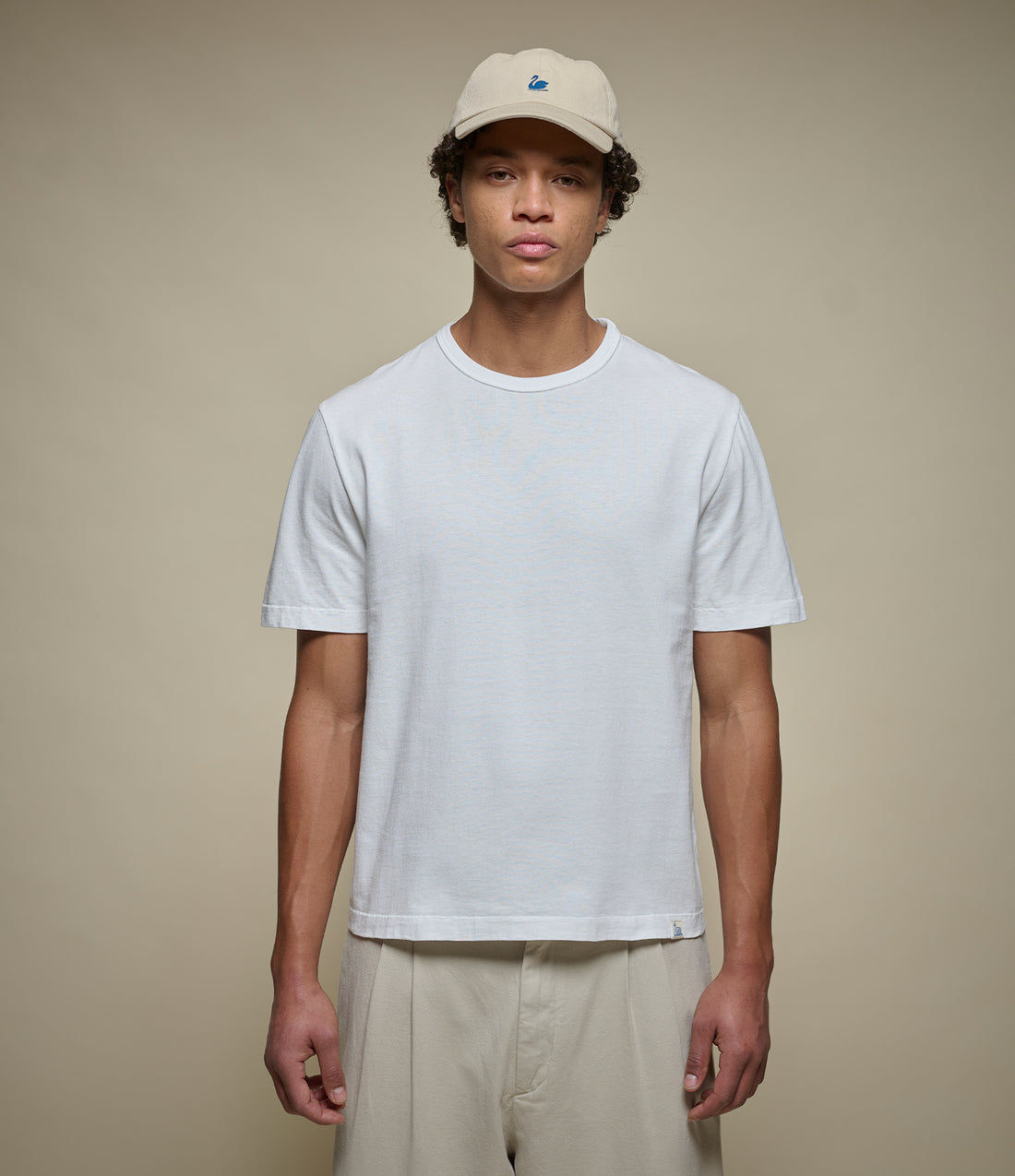 Man wearing the white TEE02C cropped tee with wide cream trousers, the hem sitting just at the waistband with the small swan tag visible