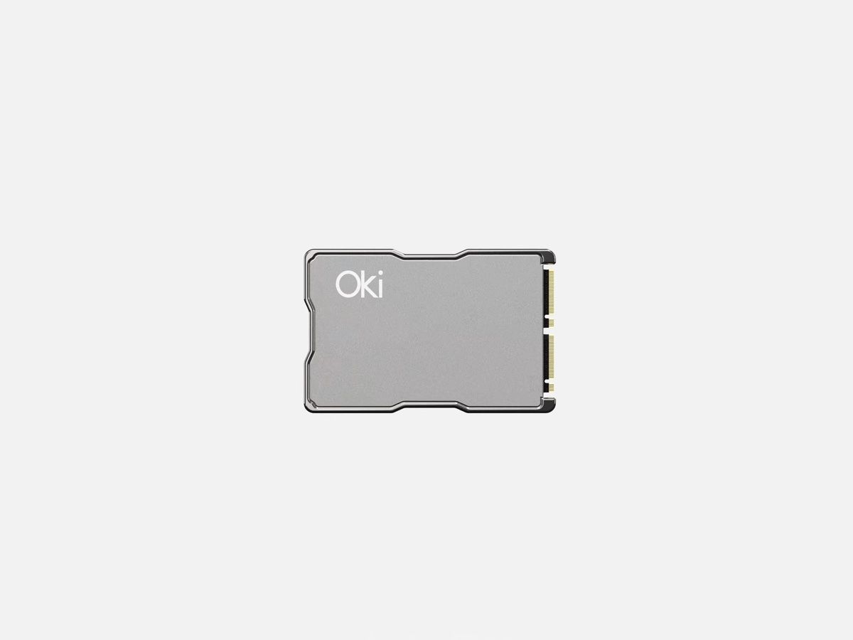 The Oki Memchip on a light grey background: a small silver card with rounded corners, the Oki wordmark in the top-left and a row of gold M.2 connector pins along its right edge