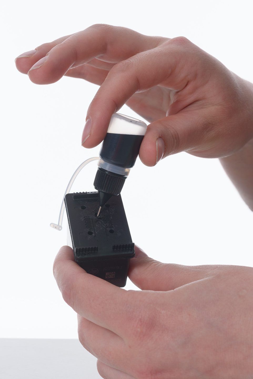 Hands refilling a black HP inkjet cartridge from a small bottle fitted with a needle tip