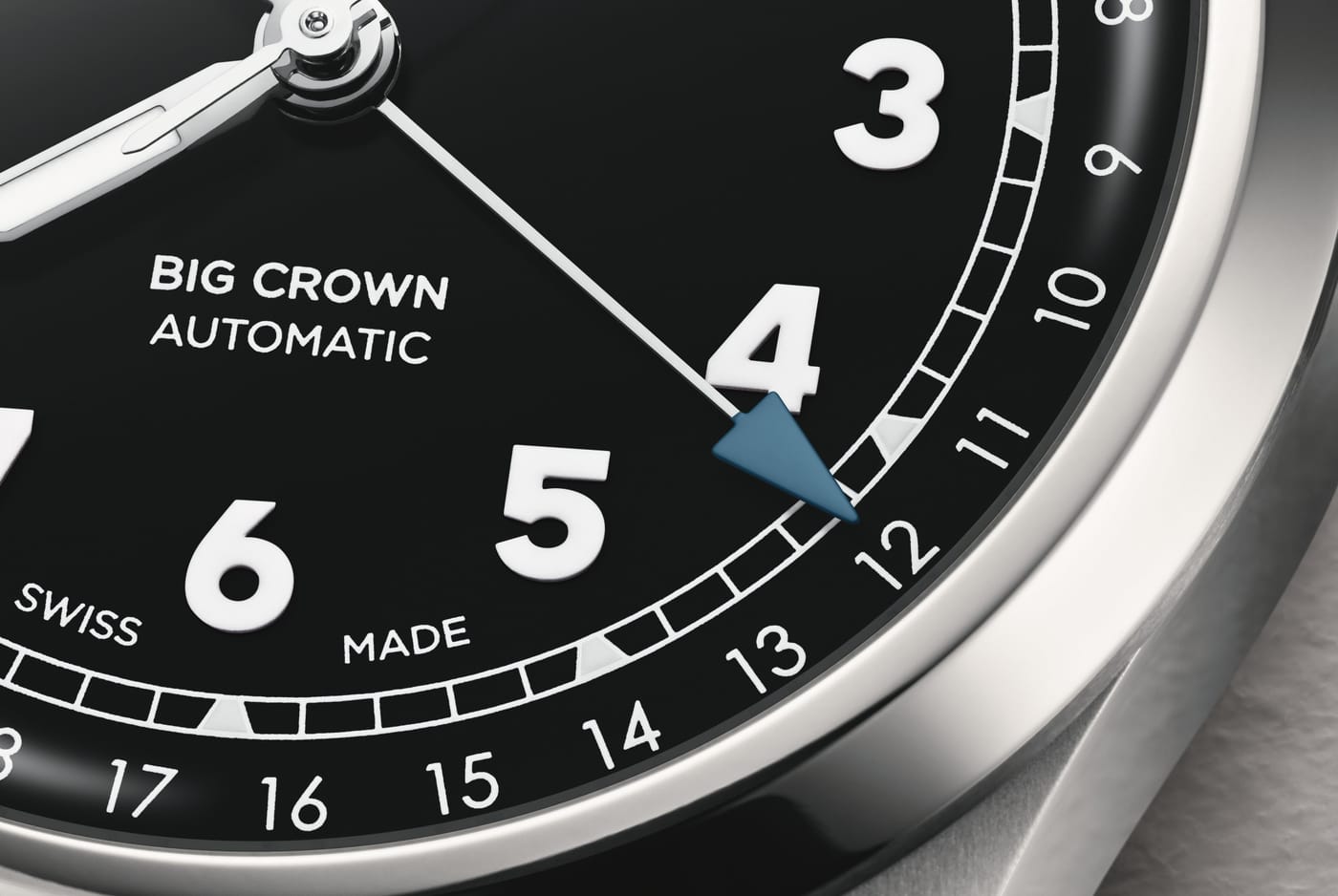 Macro of the black dial showing the blue arrow pointer-date hand aiming at the outer date ring, with applied numerals and lume triangles on the minute track