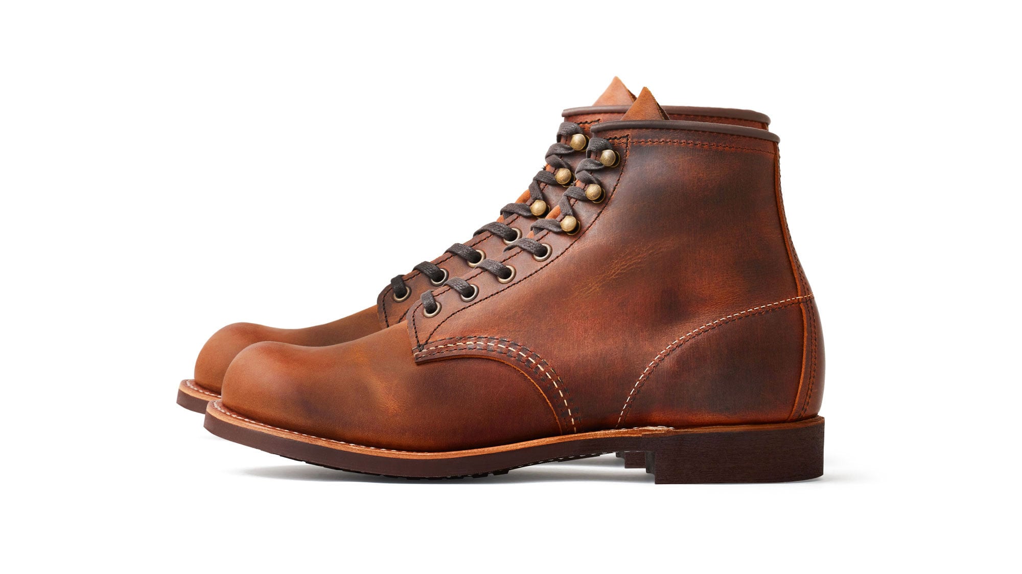 A pair of Red Wing Blacksmith 3343 boots in side view on white: copper-brown distressed leather with darker and lighter patches, a plain rounded toe, brass eyelets and speed hooks, dark brown waxed laces, a stitched welt and a dark Vibram mini-lug sole