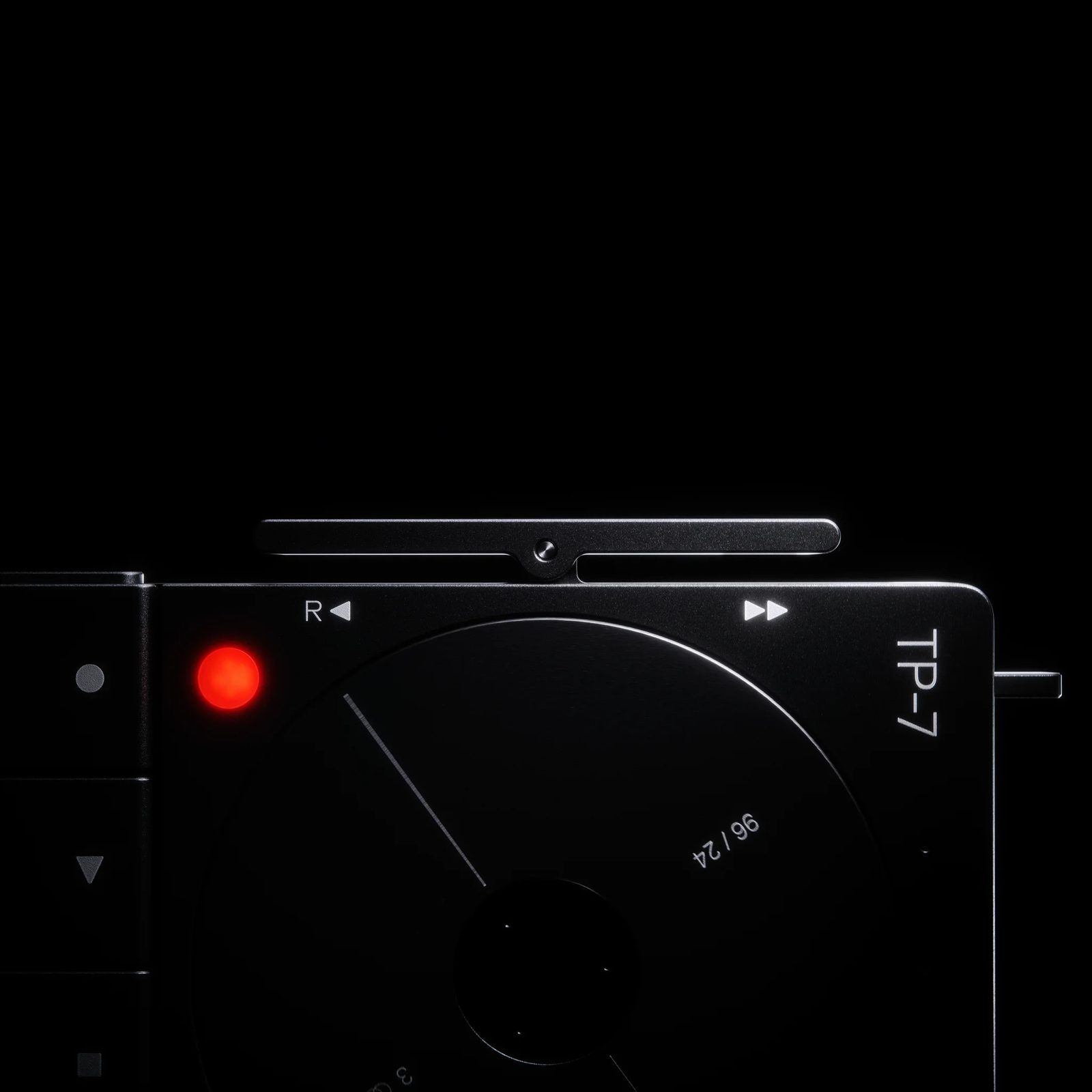 Close-up of the black TP-7: the edge of the reel wheel, the glowing red record lamp at left, and the rewind and fast-forward markings along the top