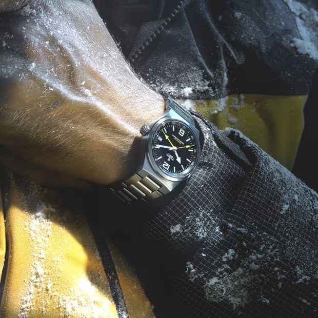 The Northflag on a wrist in snow gear, steel bracelet against a black cuff and a yellow jacket