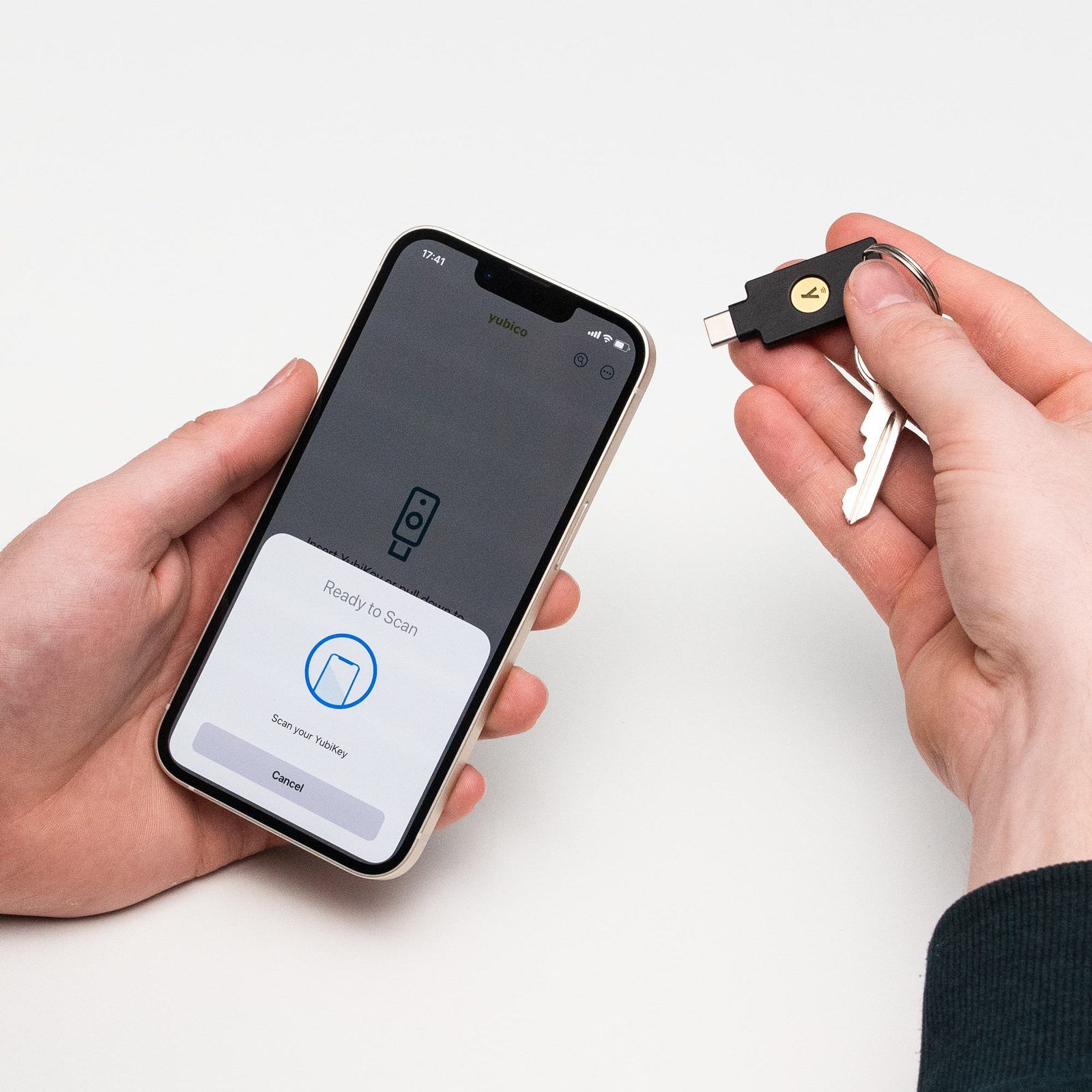 A hand holding a YubiKey 5C NFC on a key ring against the top of an iPhone, which shows a ready-to-scan prompt for the security key