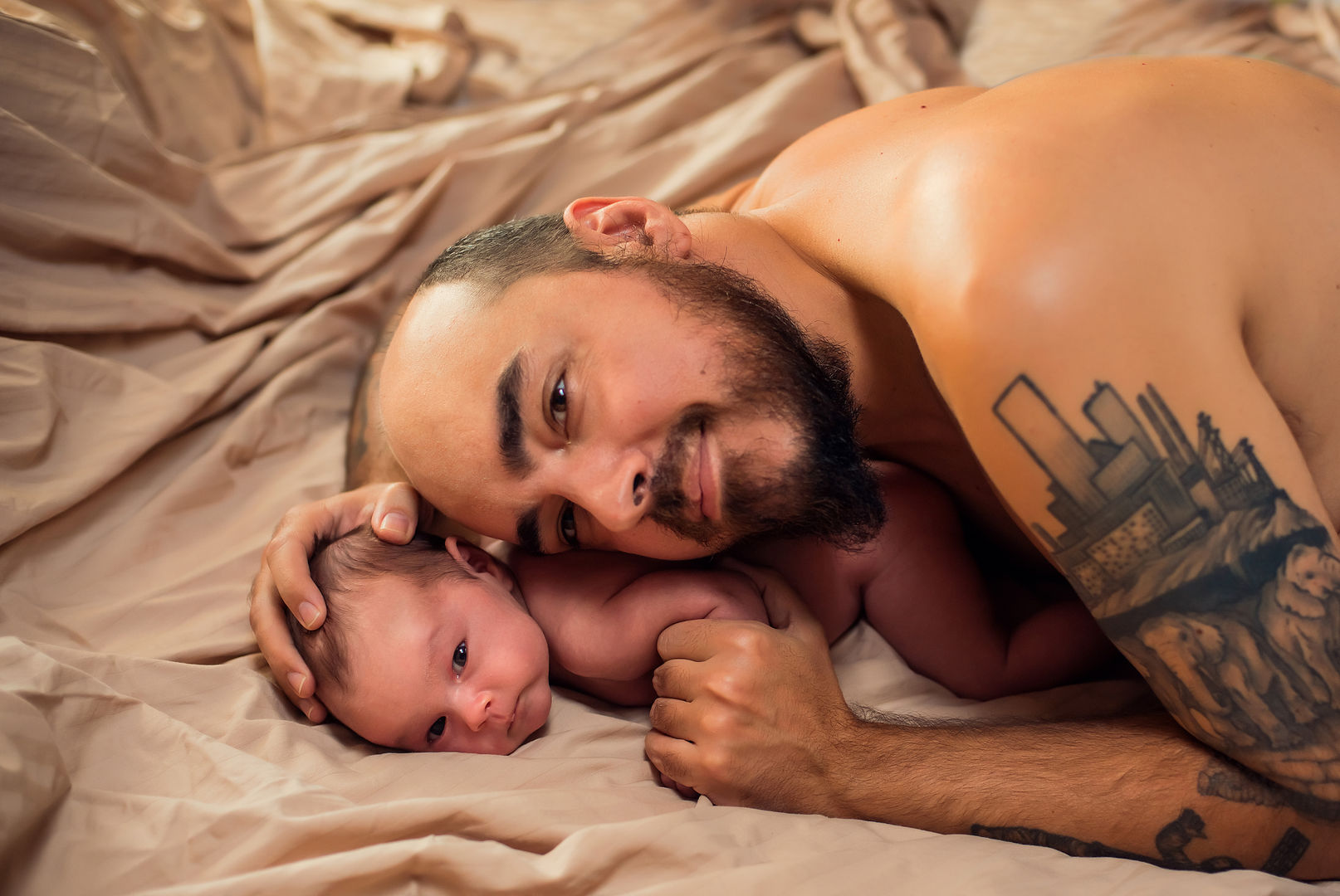Father lying with newborn baby on bed