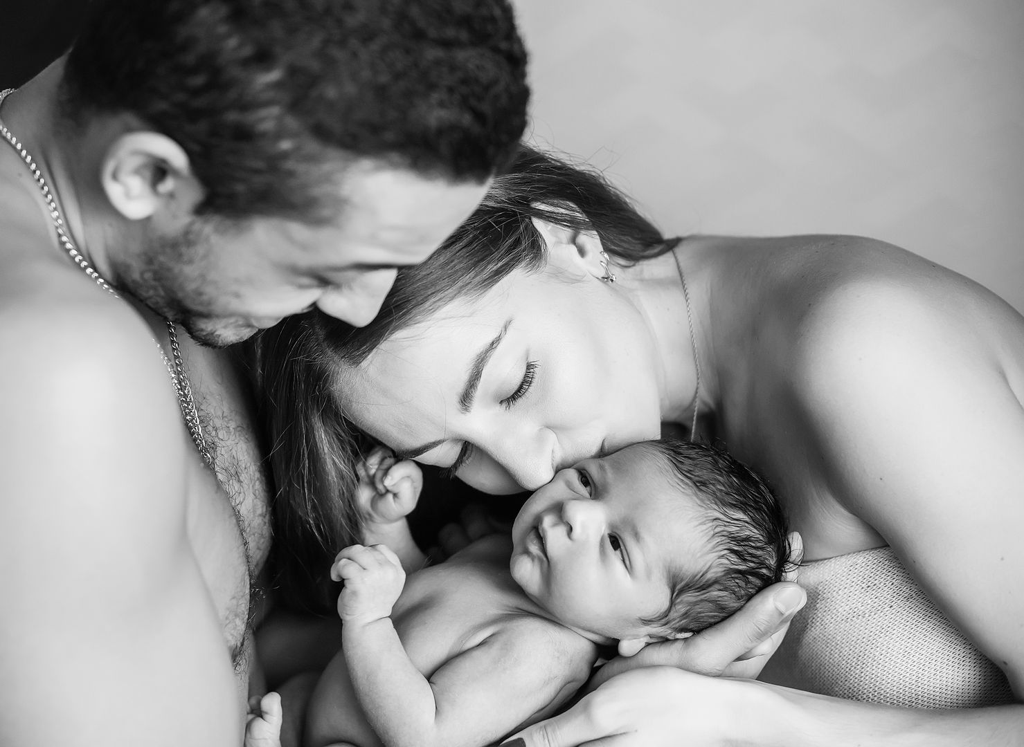Parents embracing newborn together in black and white