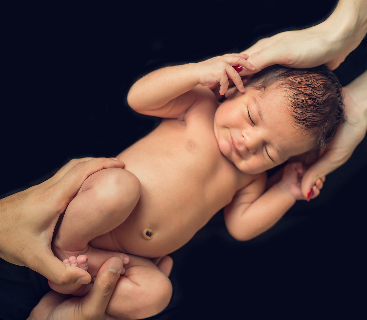 Newborn cradled by parents on black background