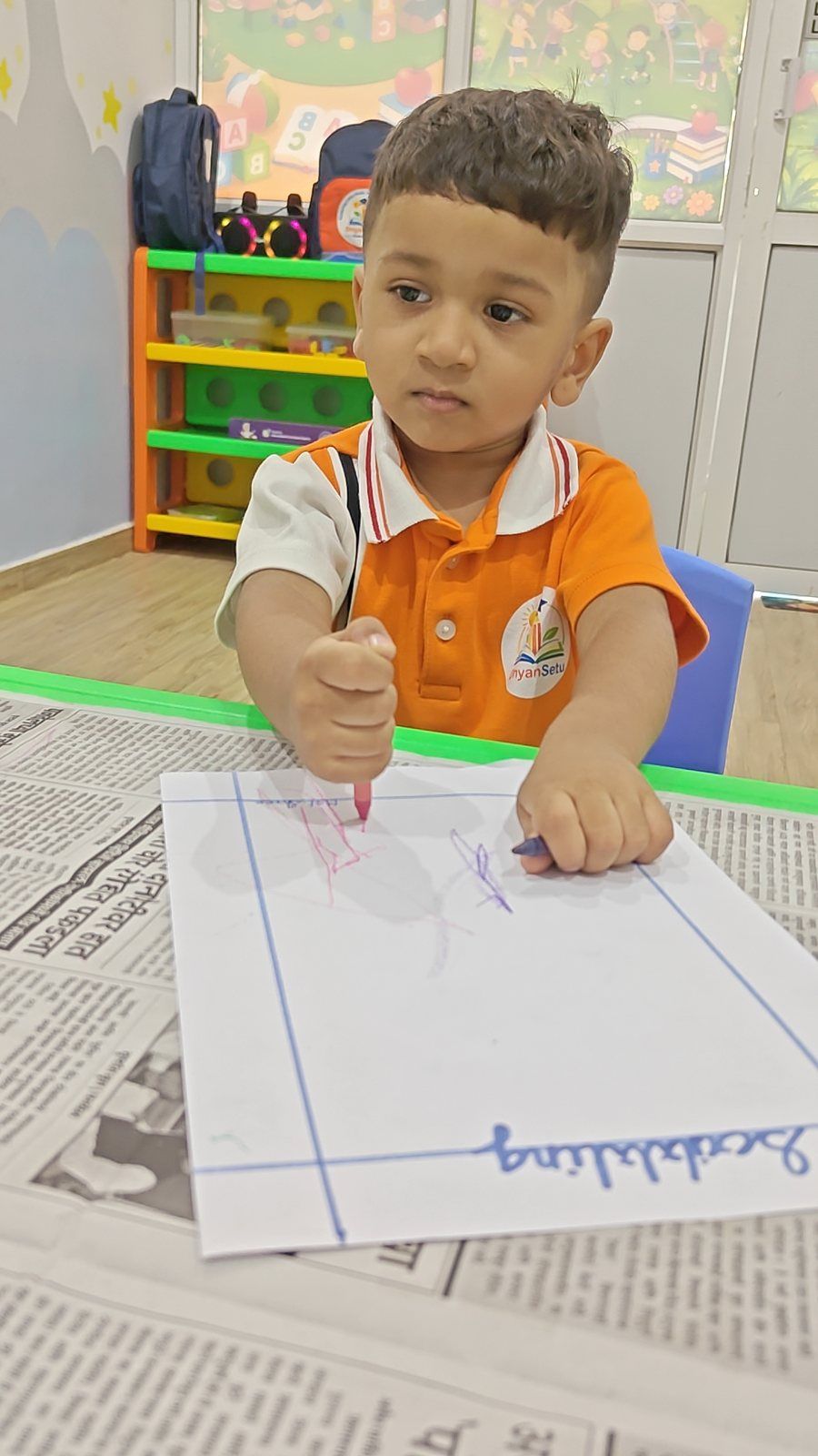 A young boy at a craft table, completely absorbed, small fist wrapped around a red crayon.