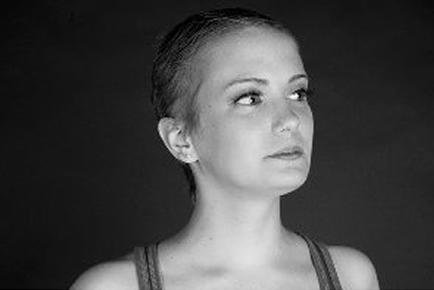 A black and white portrait of a young woman in a tank top looking thoughtfully to the side against a dark background.