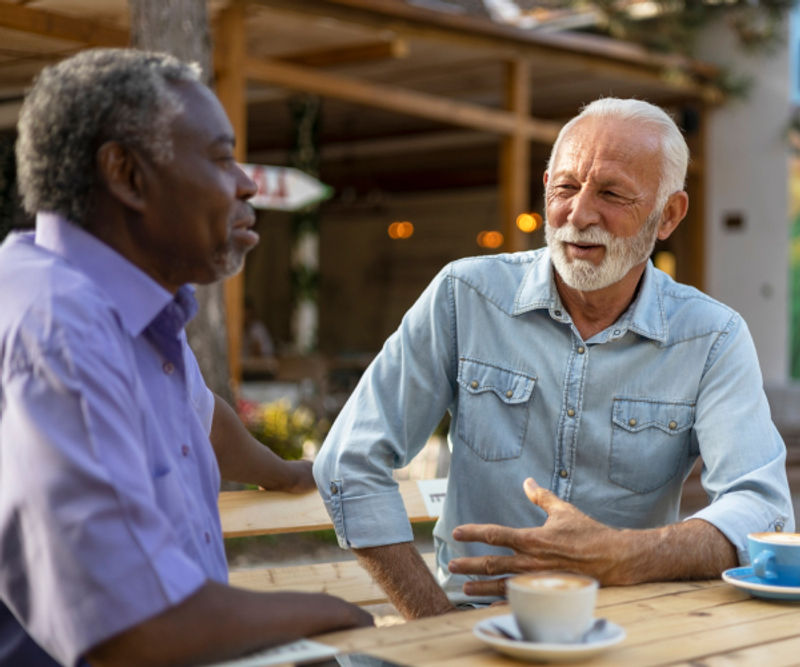 Two older members talking and having coffee together at an outdoor table.