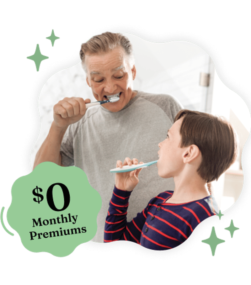 A smiling man and a young boy brushing their teeth together, framed in a wavy shape with green stars and a green badge reading '$0 Monthly Premiums'.