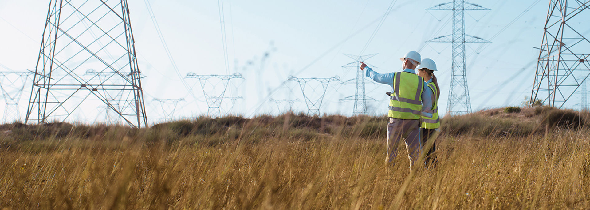 A man and woman construction working standing in a field while the man points to something in the distance