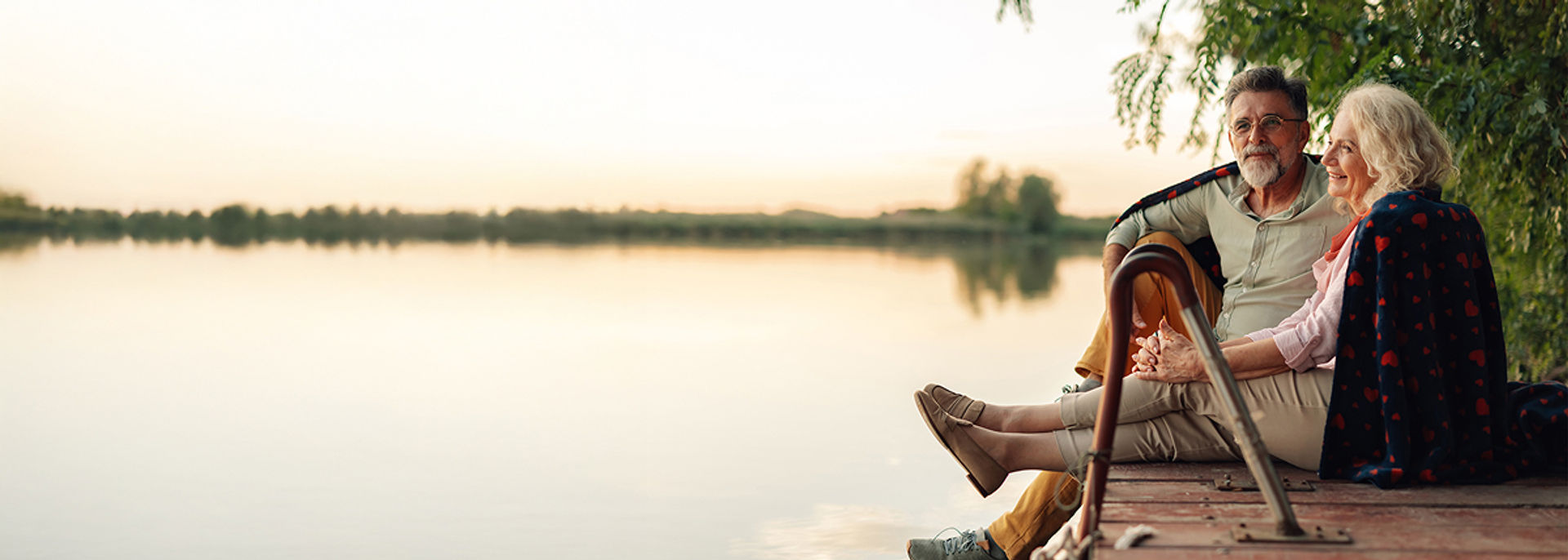 An older couple sitting on a dock by the lake watching the sunset
