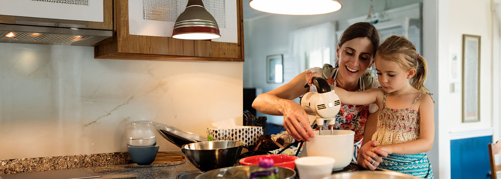 A mother and daughter in the kitchen mixing together ingredients in a bowl with a hand mixer