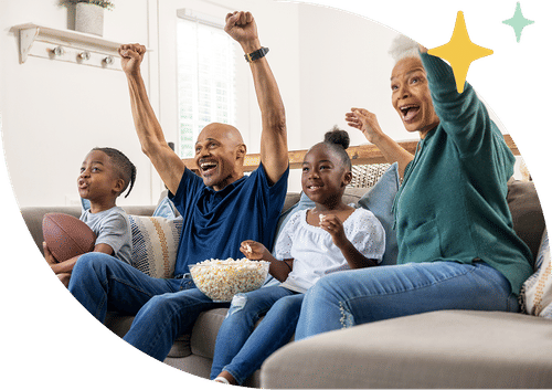 An older couple and two children cheering excitedly on a couch while watching a football game with popcorn, framed by a curved black border with decorative star graphics.