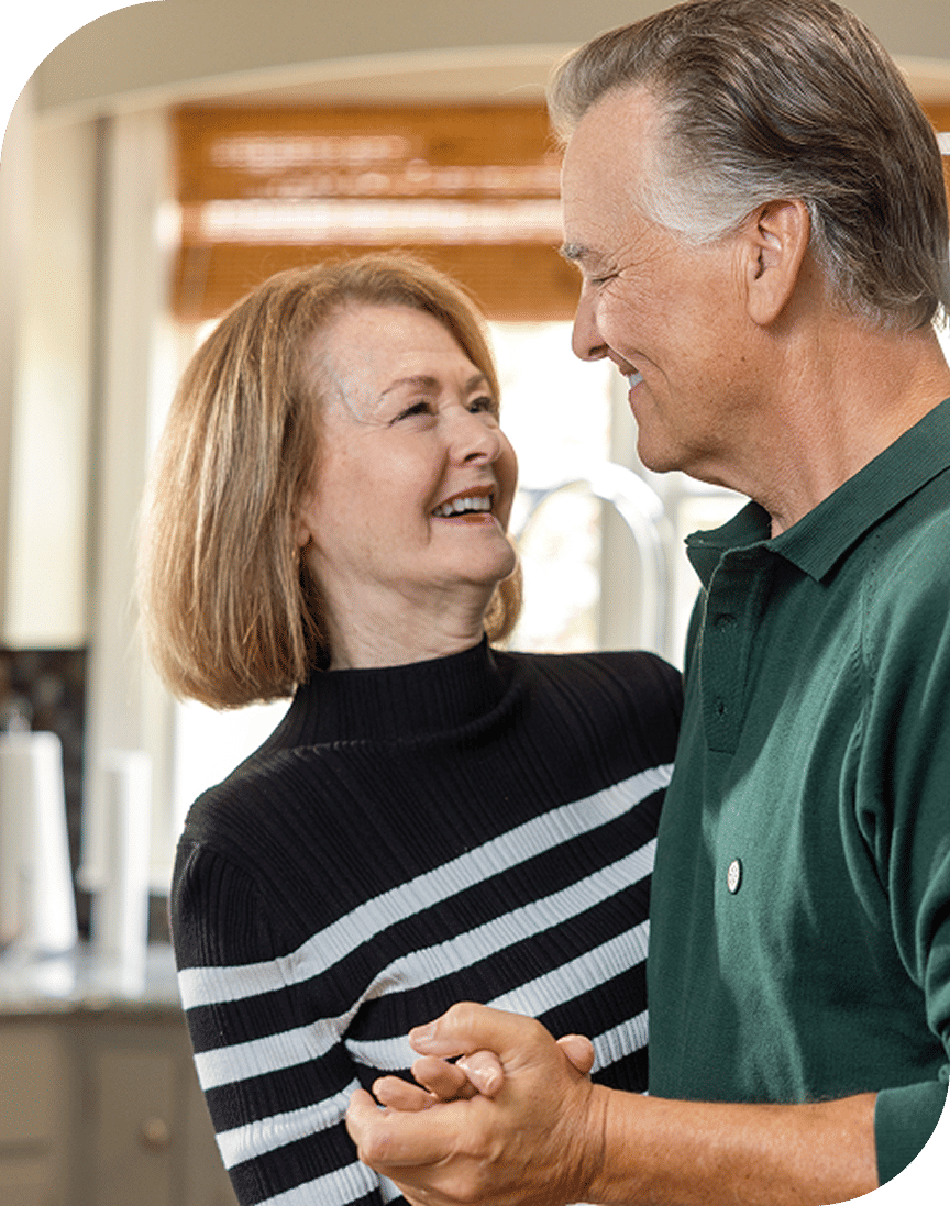 An older couple smiling and holding hands while dancing together indoors.