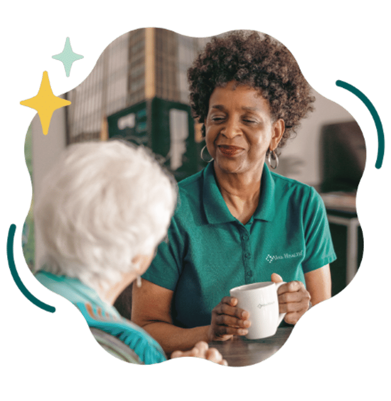 A smiling woman in a green Viva Health polo shirt holding a white mug and talking to another woman, framed by a wavy black border with decorative star graphics.