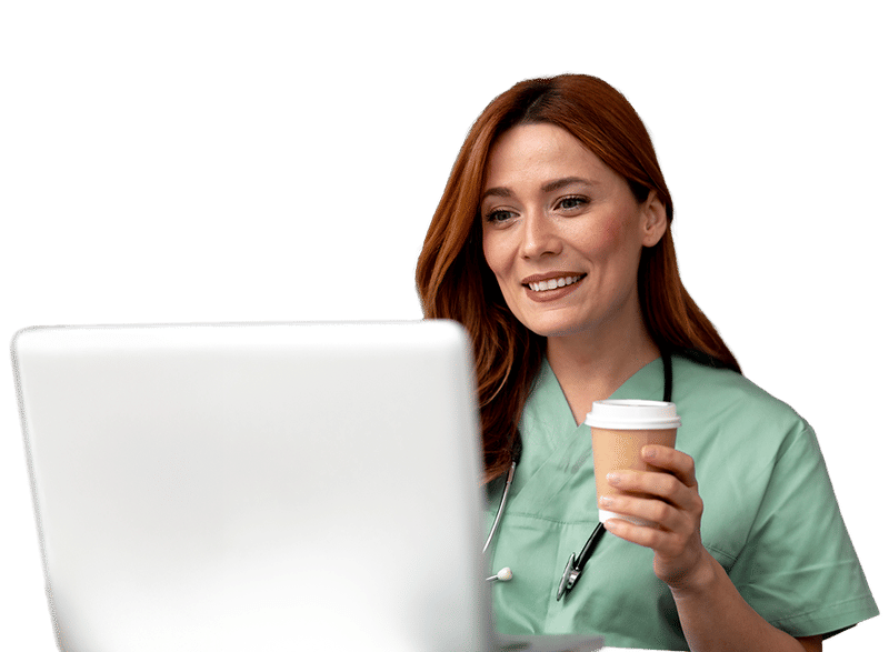 A smiling health care provider in green scrubs with a stethoscope, holding a cup of coffee while looking at a laptop screen.
