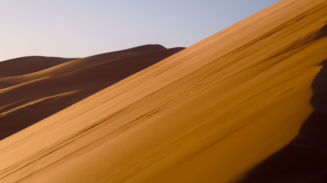Smooth dune slopes curve under warm evening light