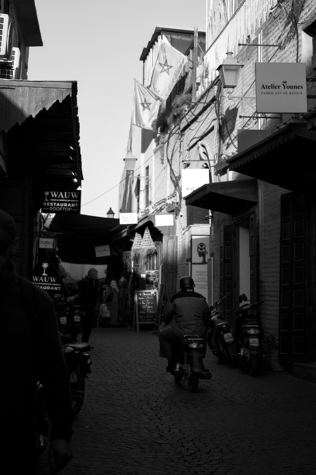 A moped rider passes beneath Moroccan flags in a medina alley