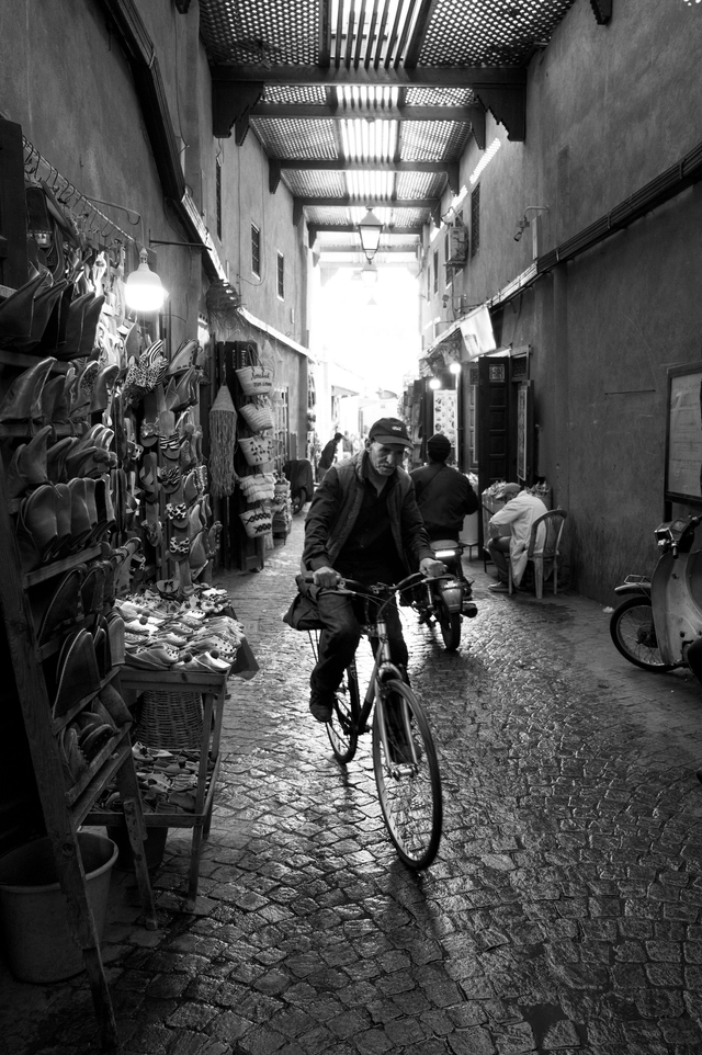 A man rides a bicycle through a sunlit medina alley