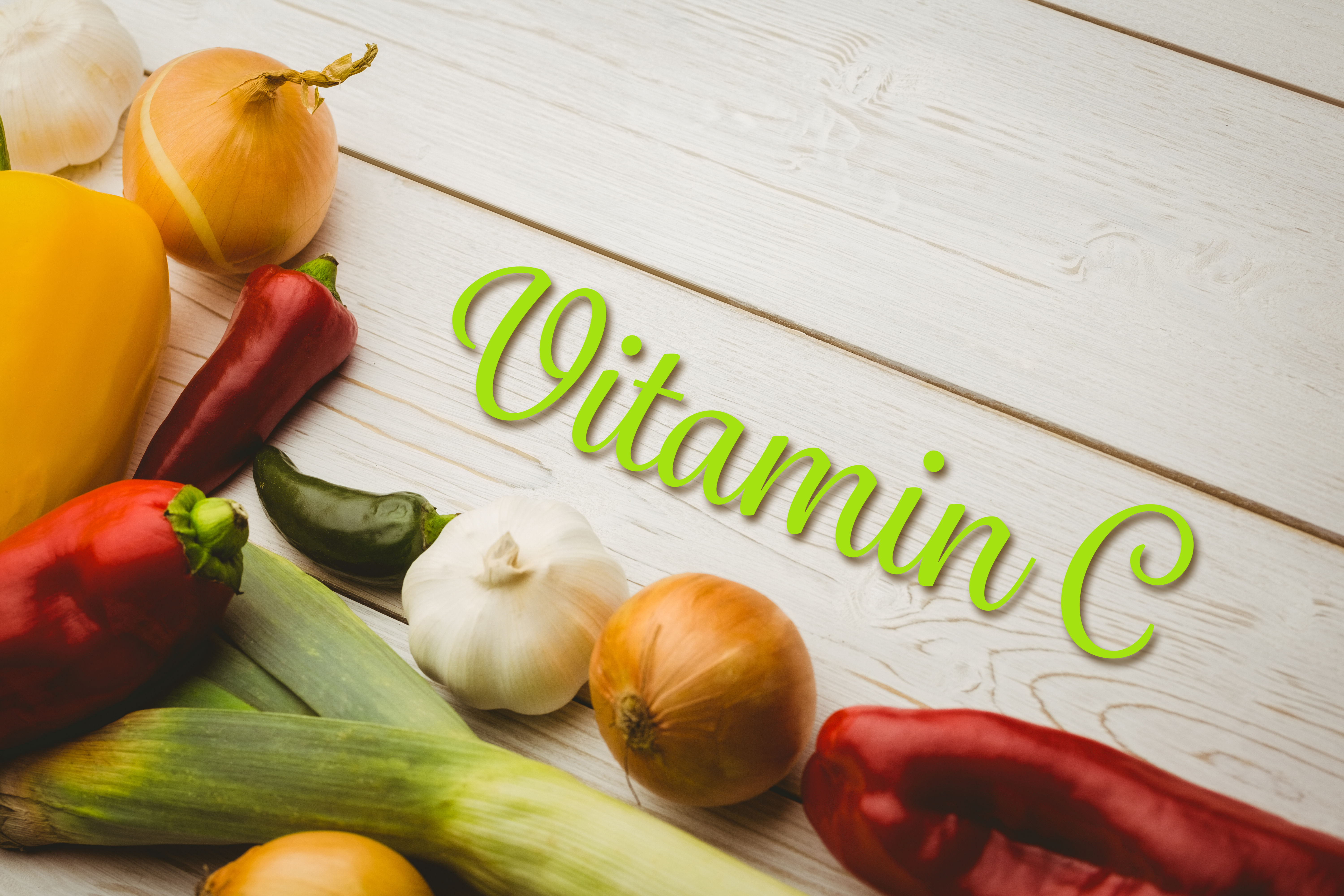 Colourful peppers, citrus fruits and fresh vegetables arranged around the words Vitamin C on a wooden surface — representing dietary and supplemental sources of vitamin C and the question of timing absorption