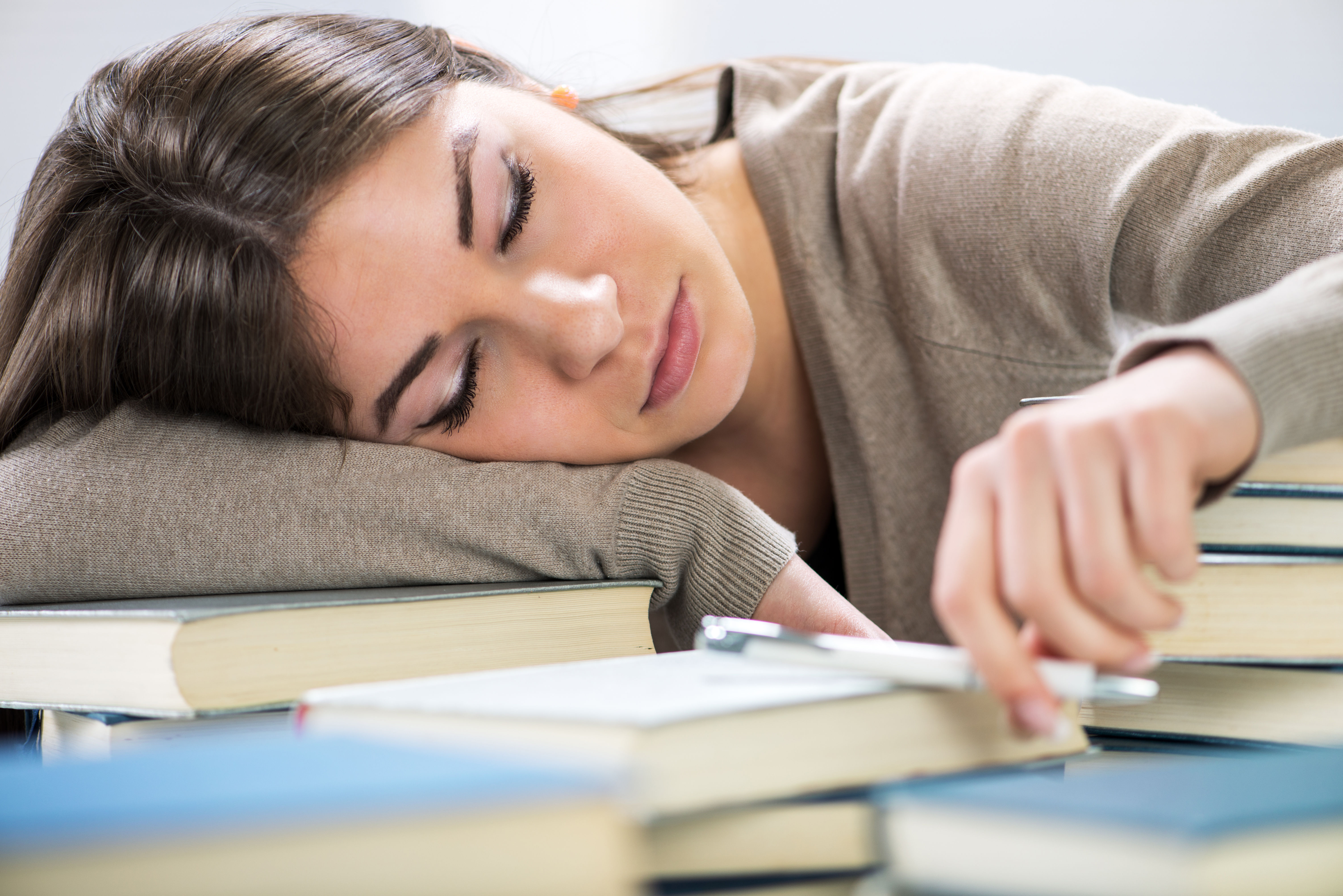 Tired student resting her head on books at a desk — fatigue affects people across every age and lifestyle, from students to working professionals