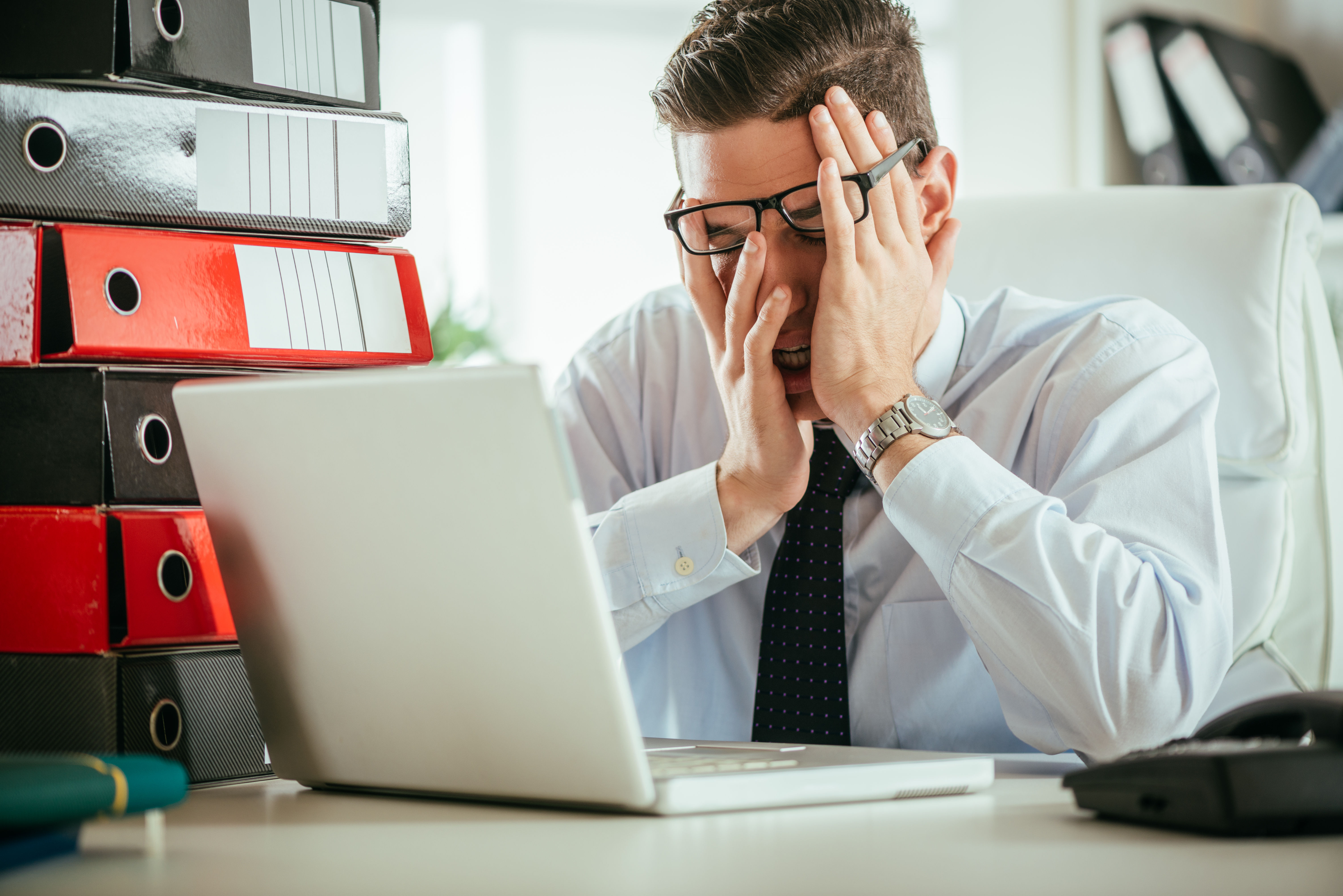 Exhausted businessman with his head in his hands at his desk — fatigue can also stem from poor sleep, chronic stress, thyroid dysfunction, or mental health, not just nutrient deficiency