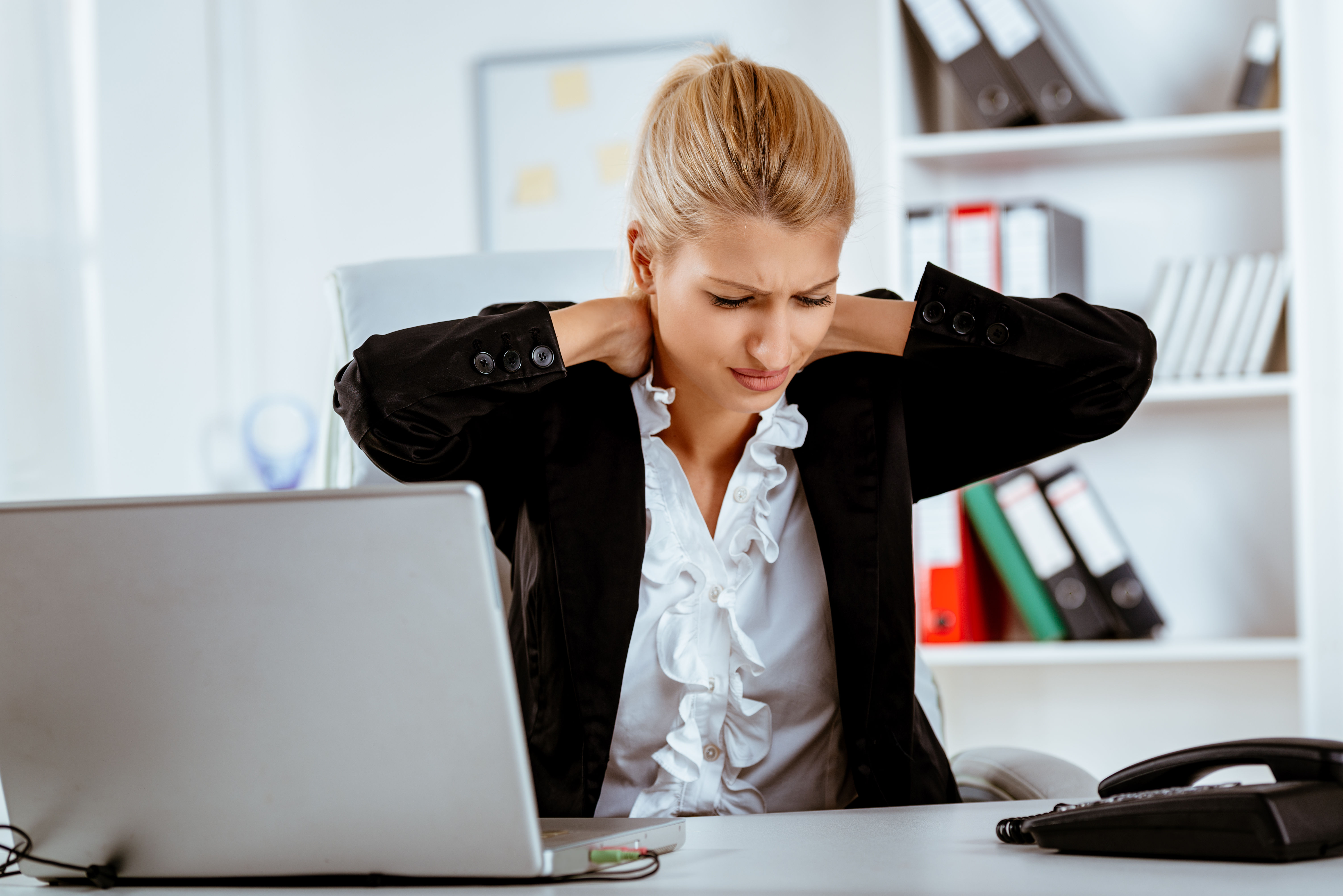 Tired businesswoman rubbing her neck at her desk — persistent fatigue is one of the most common health complaints, and a nutrient deficiency is often an overlooked but fixable cause