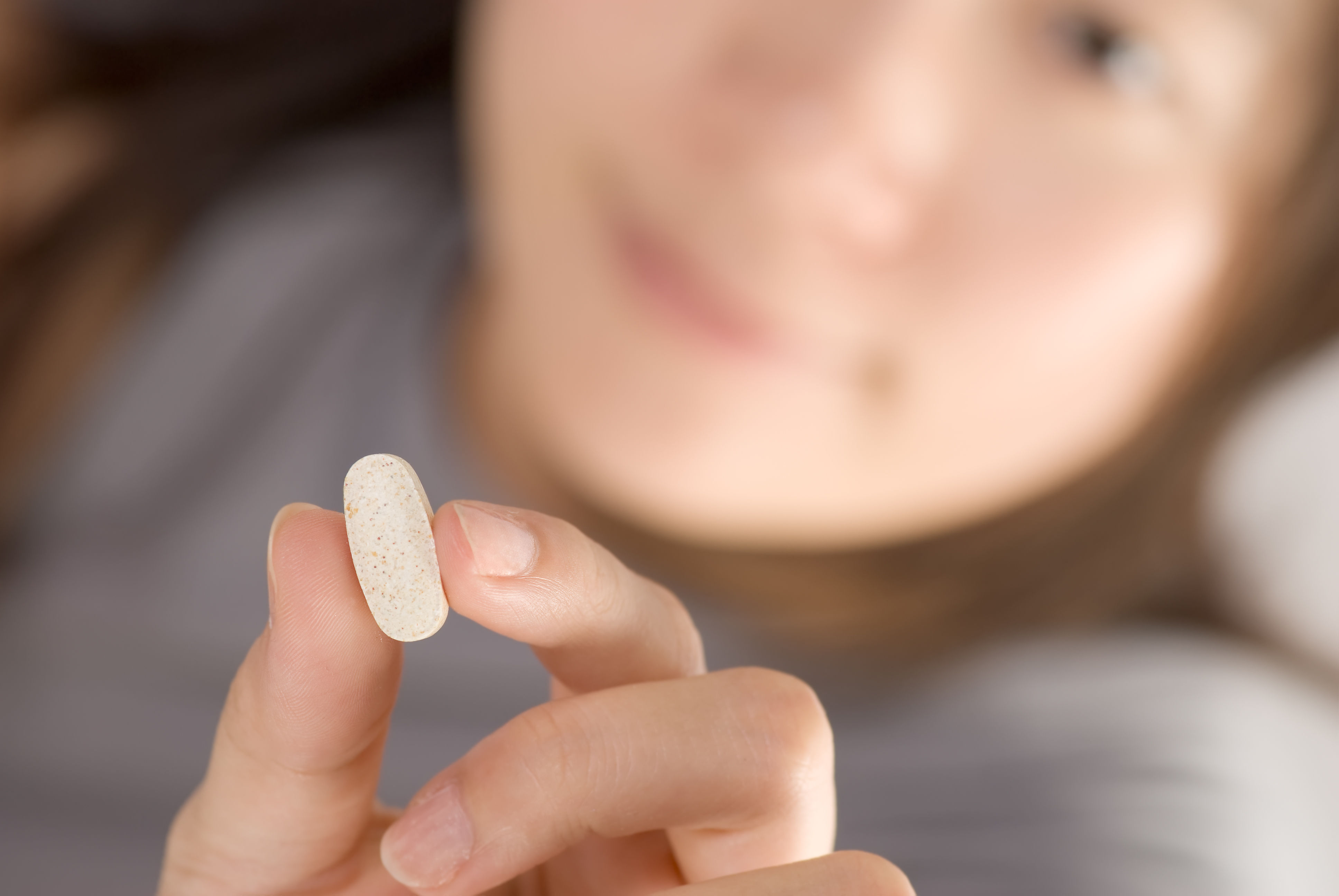 Close-up of a single vitamin pill being held between fingers — representing the bioavailability question of how much of this pill's labelled dose actually reaches the bloodstream after passing through the digestive system