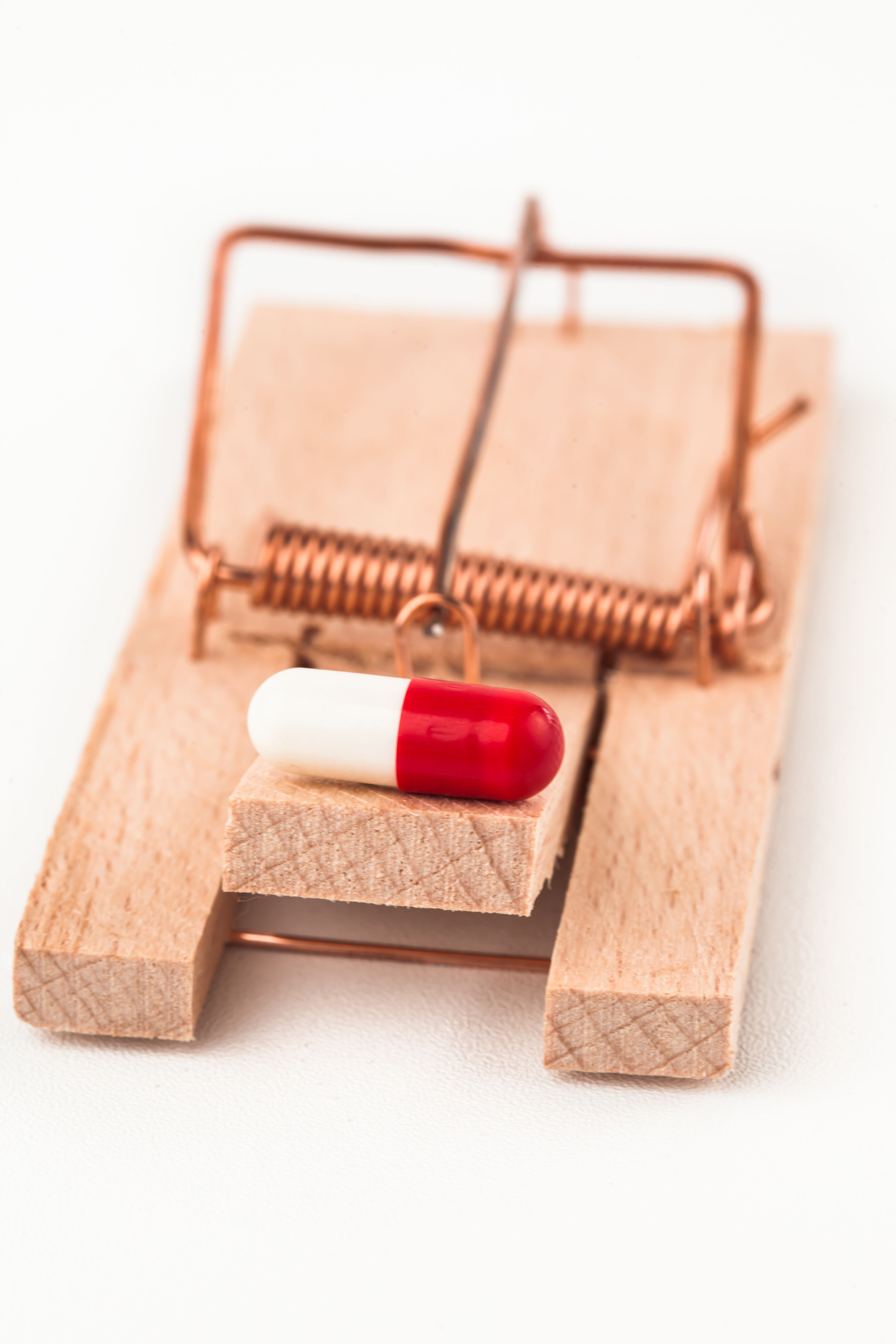 A vitamin pill caught in a mousetrap — a powerful metaphor for how the supplement industry's standard pill format traps consumers into paying for vitamins their body can barely absorb