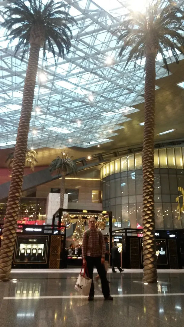 alt=""Mężczyzna stojący na lotnisku pomiędzy dwoma palmami pod przezroczystym dachem"