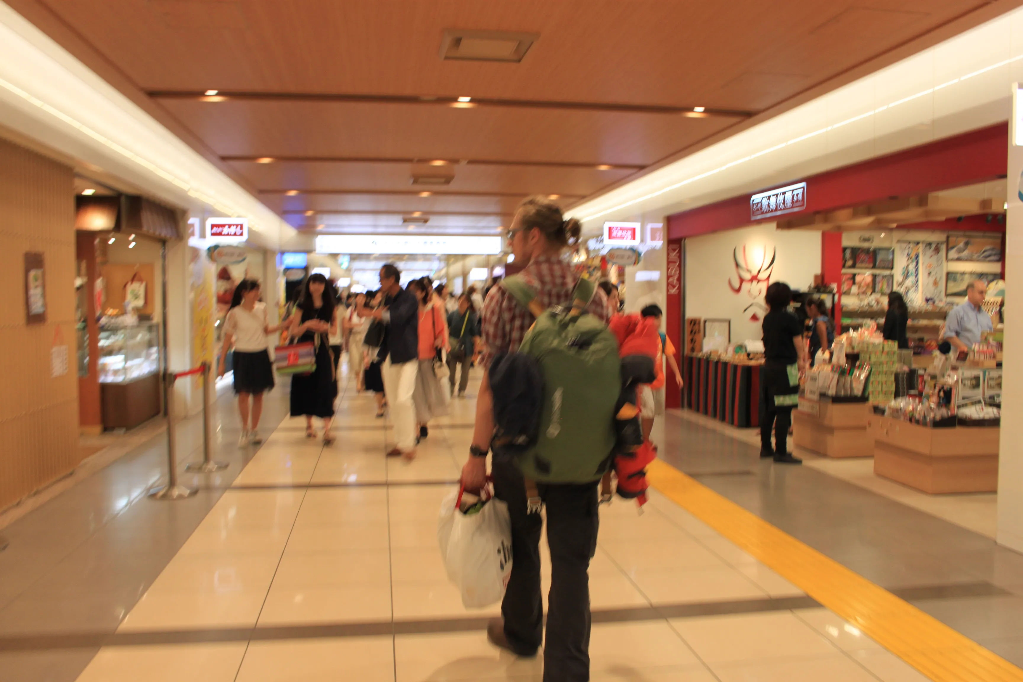 alt=Osoba z plecakiem spaceruje po korytarzach Tokyo Station City, z sklepami i innymi ludźmi