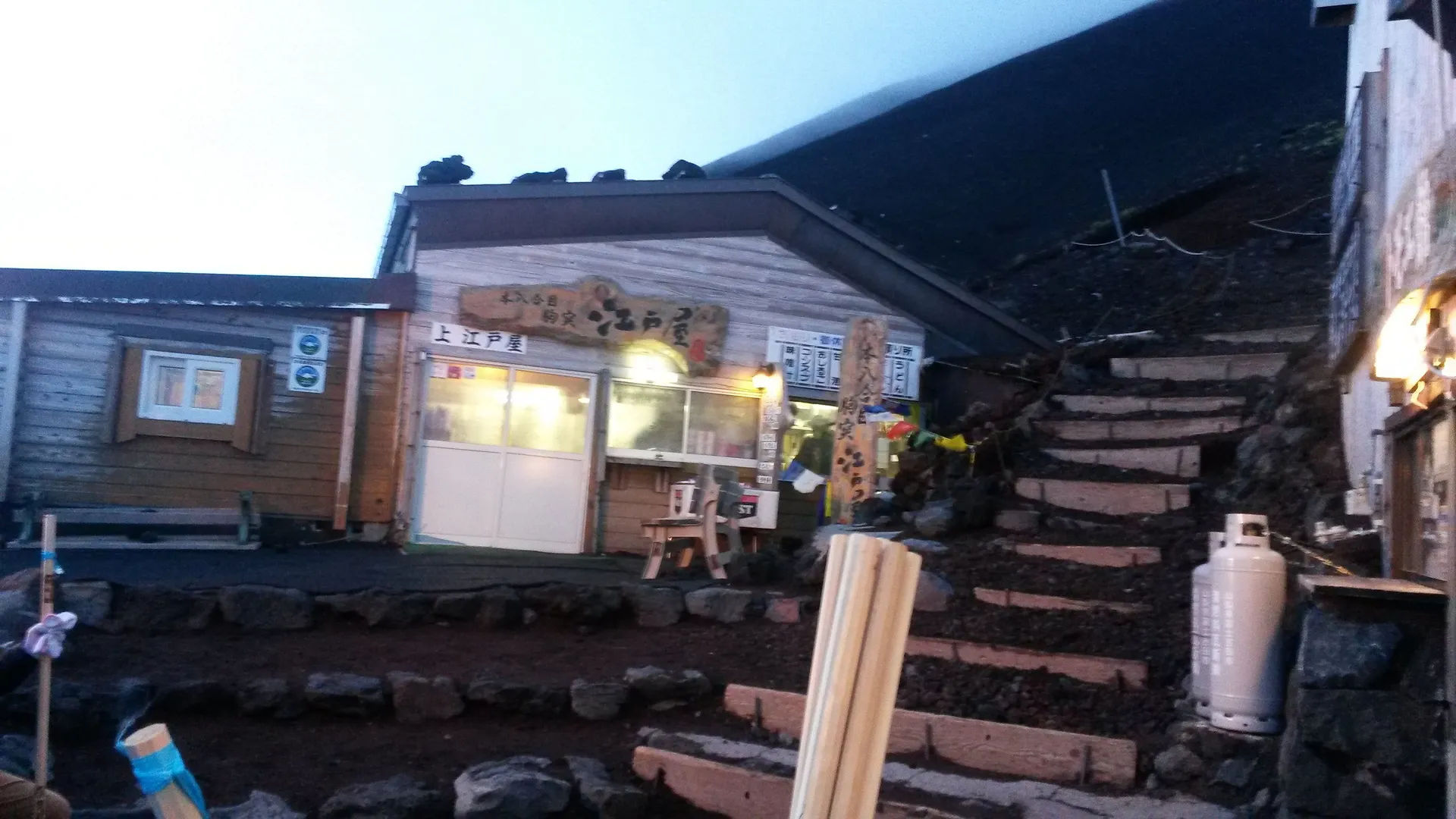 Schronisko górskie na Fuji, oświetlone w godzinach wieczornych, z widocznymi schodami prowadzącymi do wejścia.