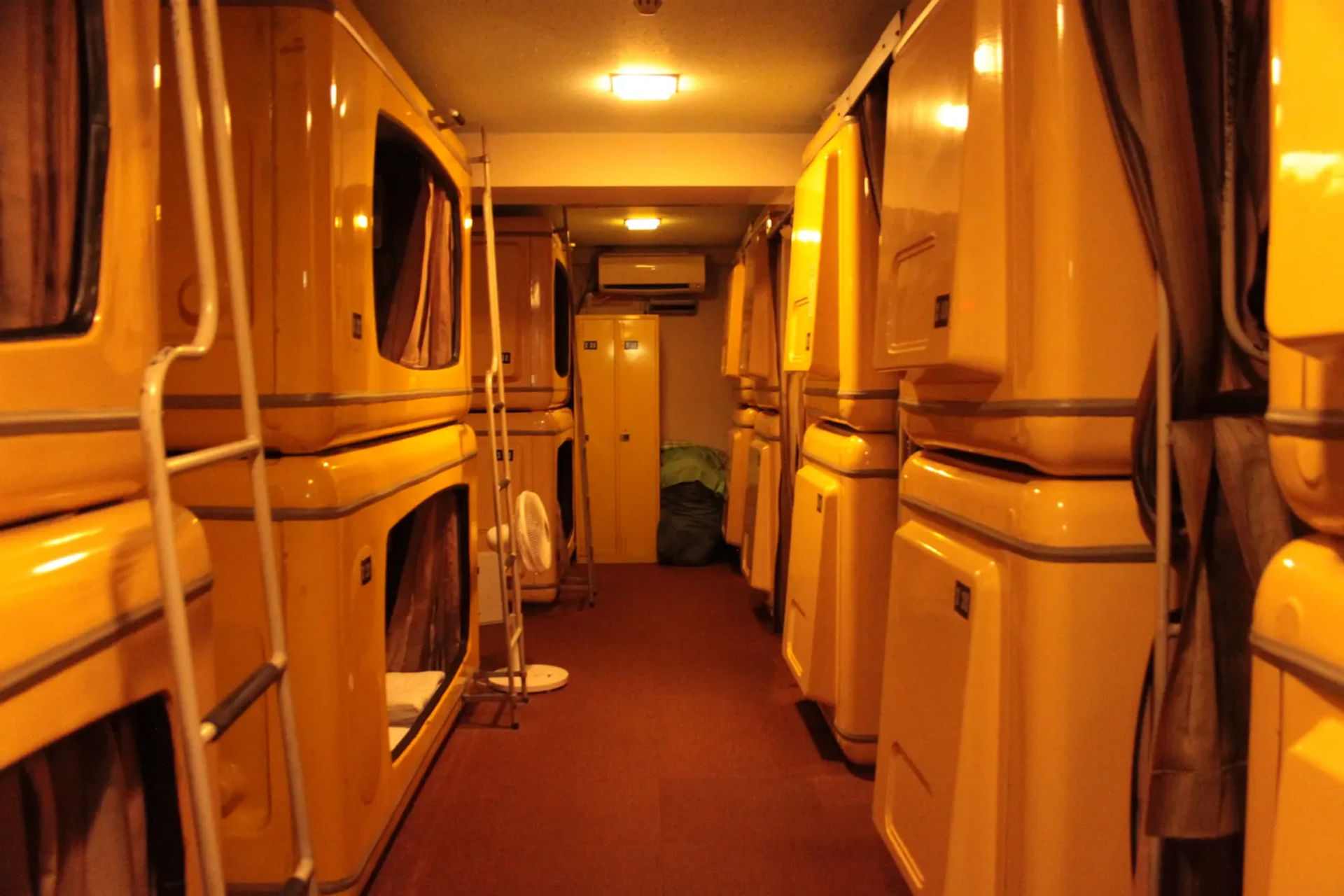 Wnętrze hotelu kapsułowego w Japonii, rząd małych kapsuł sypialnych z zasłonami, tworzących kompaktowe i funkcjonalne miejsce do spania.