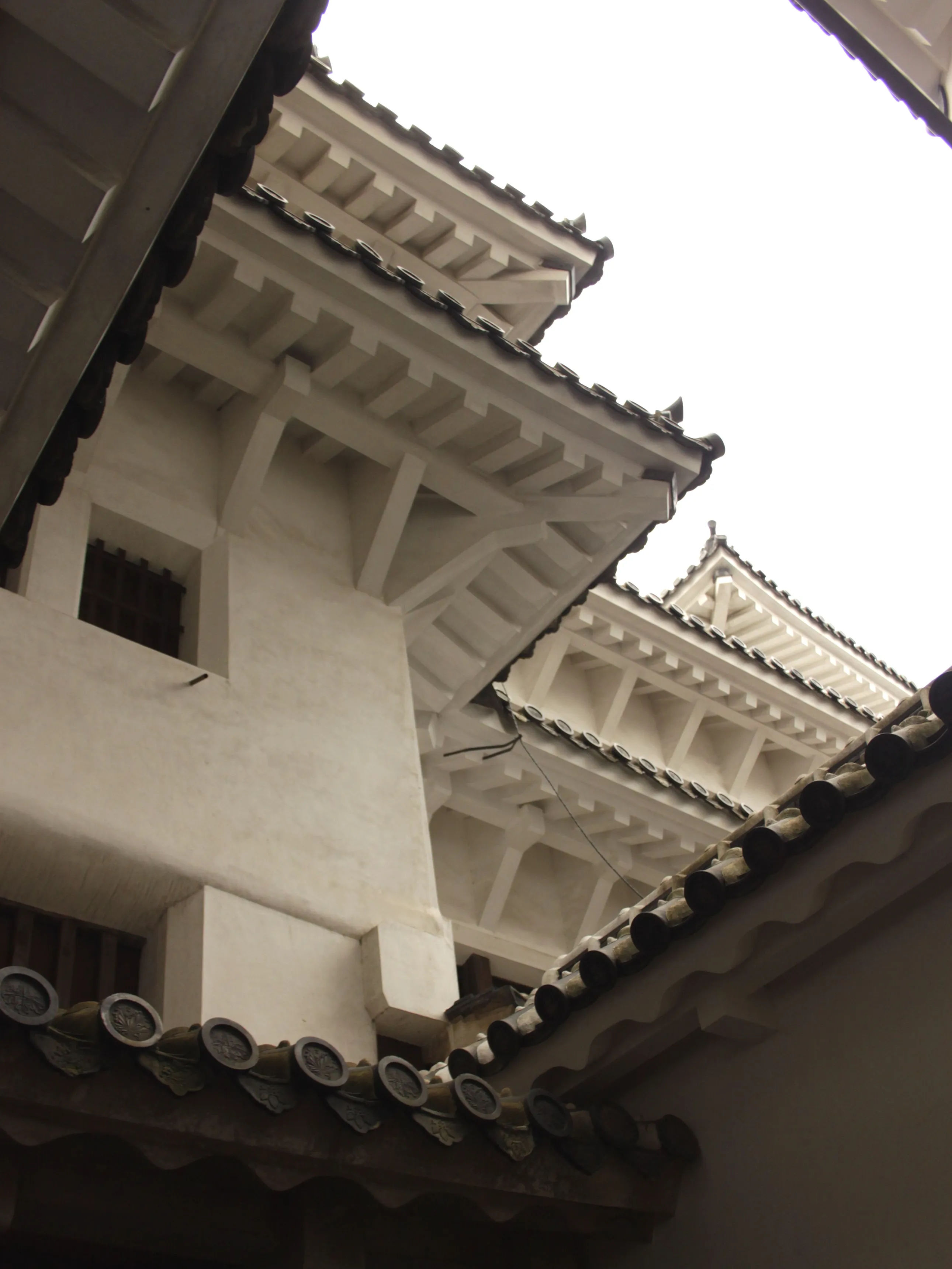 Zbliżenie na detale architektoniczne zamku Himeji, z widokiem na białe ściany i skomplikowane drewniane konstrukcje.