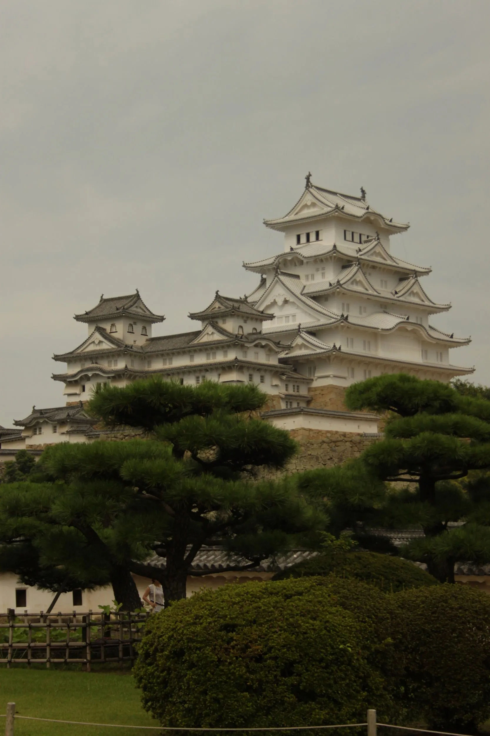 Panoramiczny widok na zamek Himeji, z otaczającymi go drzewami i błękitnym niebem w tle.
