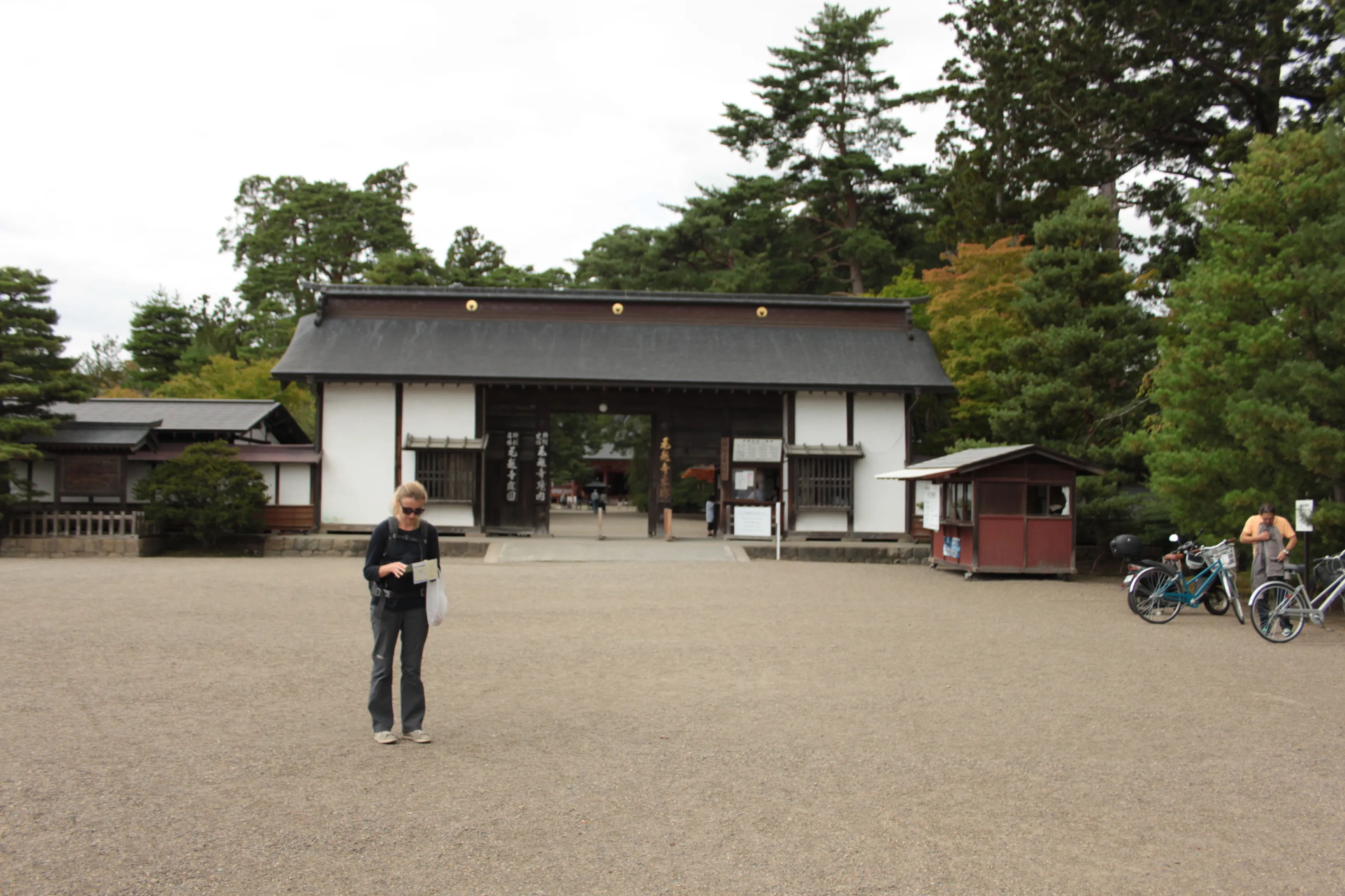 Wejście do świątyni Motsu-ji w Hiraizumi, z bramą otoczoną drzewami i turystką stojącą na placu przed wejściem